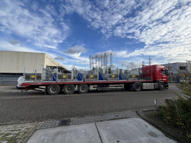 Een rode vrachtwagencombinatie van Bouwma geladen met meerdere Warry bouwliften voor transport naar een bouwlocatie.